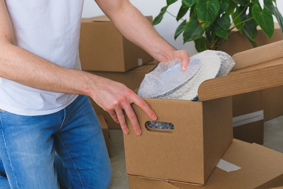 A wooden table inside a home or office space, covered with various packing materials used for delicate items. There are multiple large sheets and rolls of bubble wrap, some partially unrolled and crum